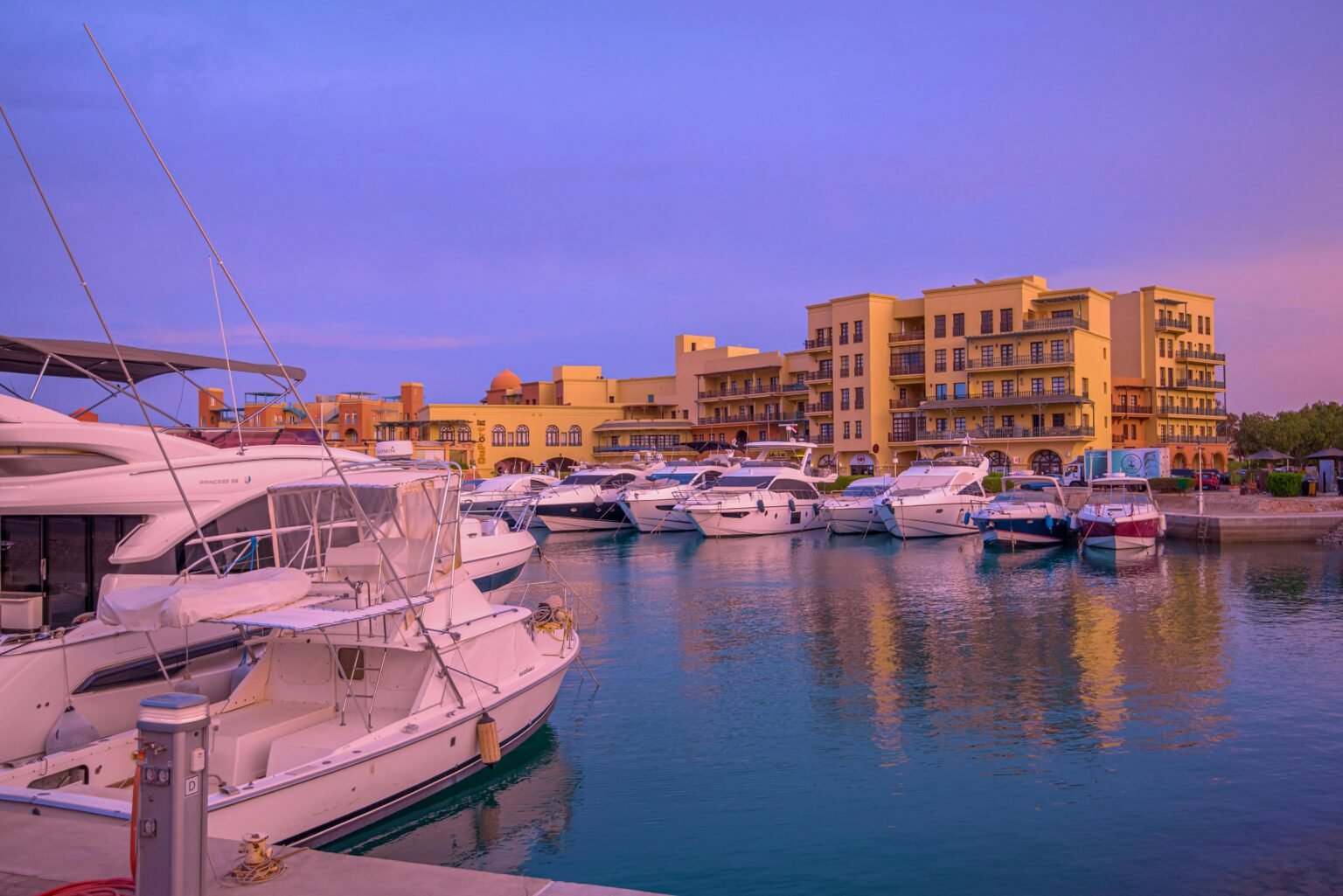 A serene view of luxury yachts docked at Hurghada Marina during sunset, showcasing vibrant architecture.